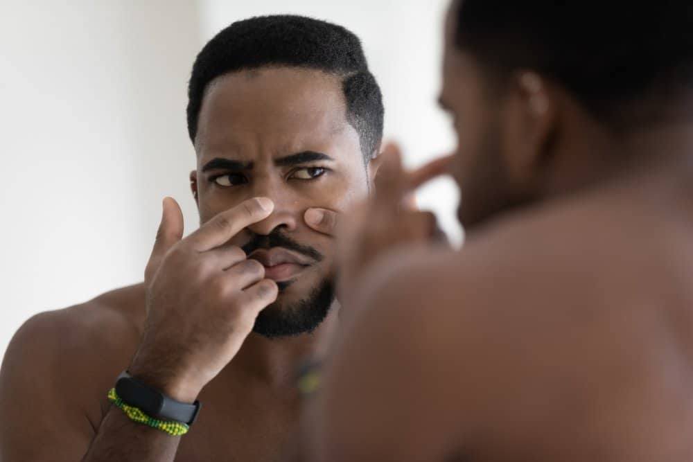 Serious,Discontented,African,Guy,Looking,In,Mirror,Touches,Face,Squeezes